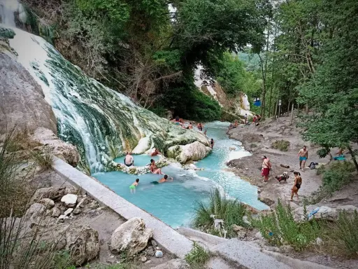 Cascata bianca e pozze azzurre alle terme San Filippo, con persone che si rilassano nell'acqua termale.