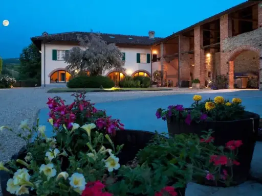 Un casale illuminato al crepuscolo, con fiori colorati in primo piano. Ideale per un weekend degustazione vini Piemonte.