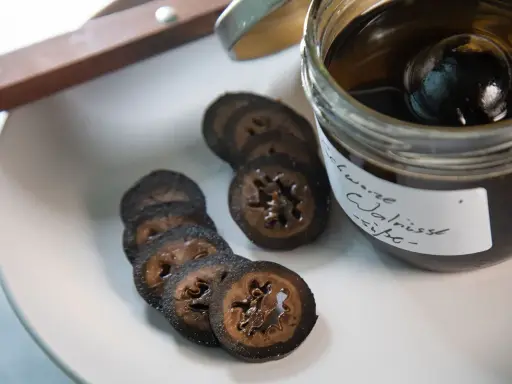 Schwarze Walnüsse in Sirup, bereit für ein köstliches schwarze walnuss rezept. Auf einem Teller liegen geschnittene Scheiben.