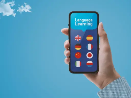 Dłoń trzyma smartfon z aplikacją do nauki języków. Wybór między Busuu czy Duolingo? Na ekranie flagi: UK, Hiszpanii, Niemiec, Francji, Chin, Japonii, Włoch, Polski.