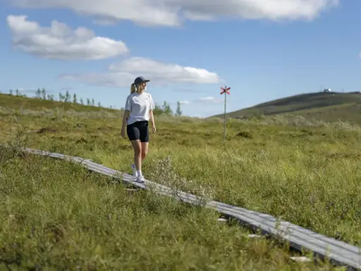 Kvinna vandrar på spång i Gällivare, Sverige. En röd markering syns i bakgrunden.