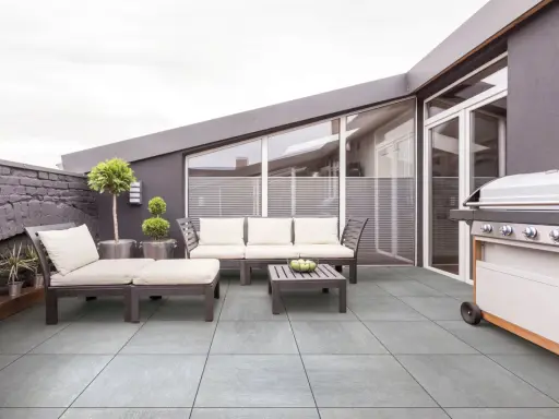 Terrasse moderne avec mobilier de jardin et barbecue. Le carrelage extérieur antidérapant est facile à nettoyer.