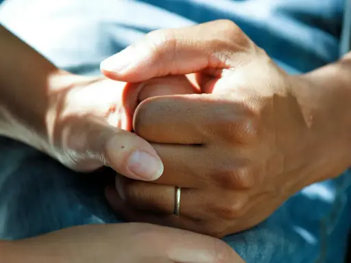 Två händer håller varandra, en gest som visar medlidande och stöd. En tunn ring syns på ena handen.