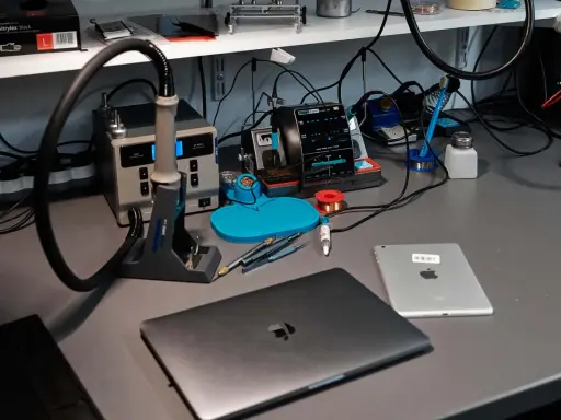 Na biurku serwisowym leży zamknięty laptop, obok tablet. W tle widać stację lutowniczą i narzędzia.