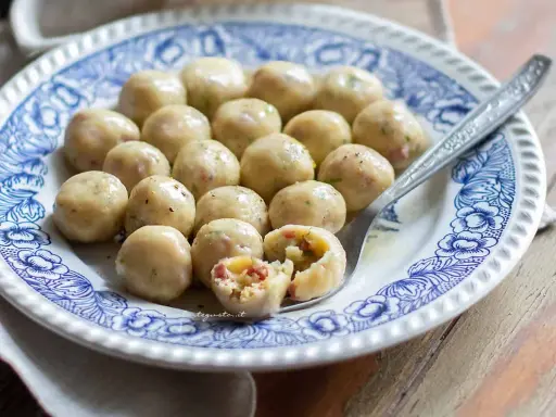 Gnocchi di pane su piatto decorato, uno spezzato rivela un ripieno saporito.