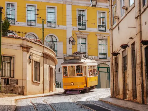 Gelbe Straßenbahn fährt durch enge Gassen Lissabons. Perfekt für angenehme Portugal Temperaturen im Mai.