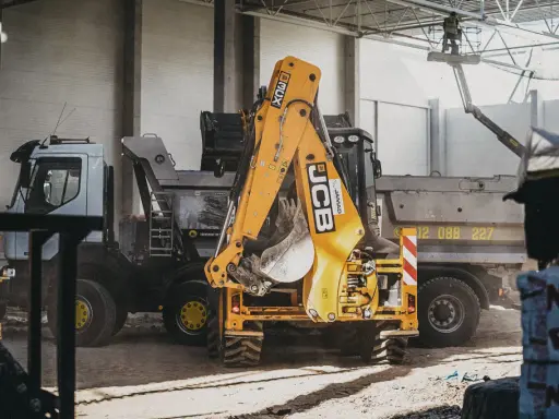 Żółty koparko-ładowarka JCB i ciężarówka na placu budowy.