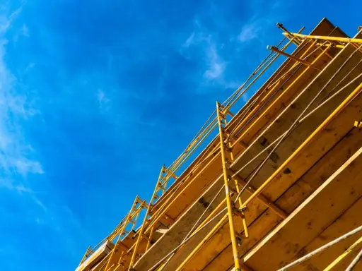 Estructura amarilla de madera y metal, que es una cimbra, contra un cielo azul con nubes finas.