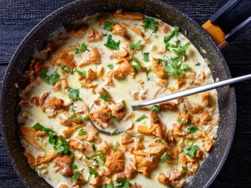 Pfifferlinge in cremiger Rahmsauce, garniert mit frischer Petersilie, in einer Pfanne. Ein Löffel ragt aus der köstlichen Speise.