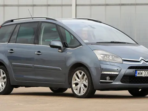 Szary Citroen Picasso z napisem "Picasso" na błotniku, zaparkowany przed budynkiem.