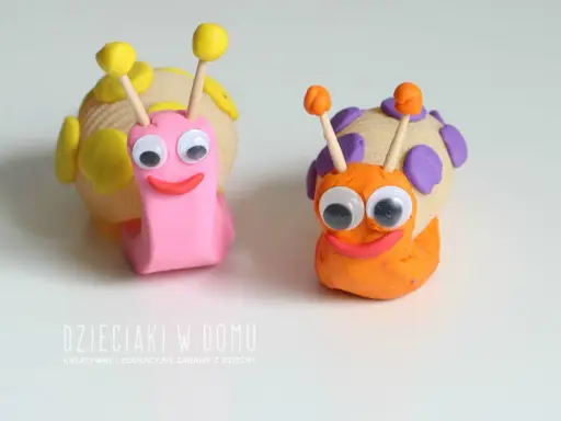 Dwa urocze ślimaki z plasteliny, jeden różowy, drugi pomarańczowy, z wielkimi oczami i uśmiechem.