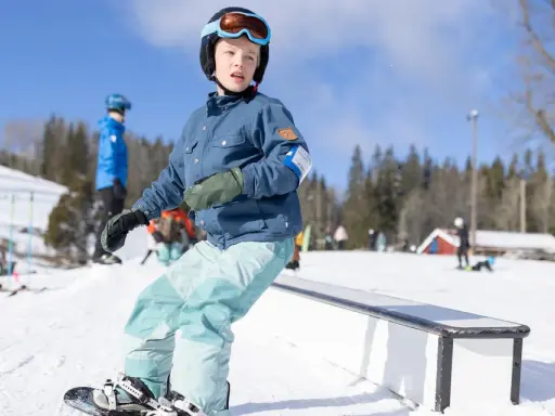 Barn åker snowboard i backen, redo att åka slalom. Solen skiner och snön ligger djup.