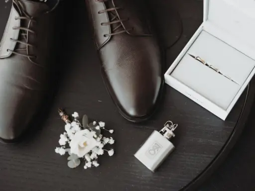 Eleganckie brązowe buty męskie, butonierka, pierścionki w pudełku i piersiówka.