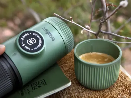 Kawa w górach: nanopresso i filiżanka świeżego espresso na drewnianym pniu, otoczone leśną scenerią.