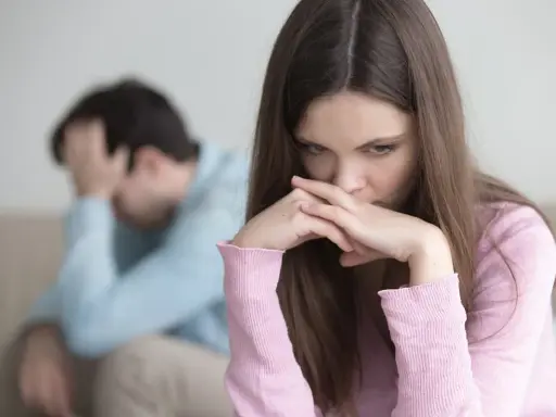Zmartwiona kobieta z dłońmi przy ustach, obok mężczyzna z ręką na głowie. W tle widać kanapę. Obraz symbolizuje **relationship ocd**.