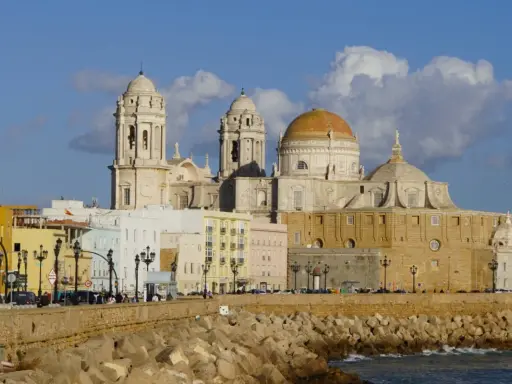 Die Kathedrale von Cadiz, ein majestätisches Bauwerk mit goldenen Kuppeln, ragt über bunte Häuser am Meer auf.