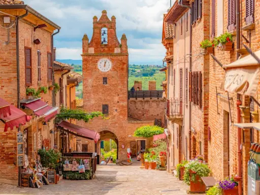 Un vicolo pittoresco a Gradara e dintorni, con case in mattoni, negozietti e un'antica torre dell'orologio.