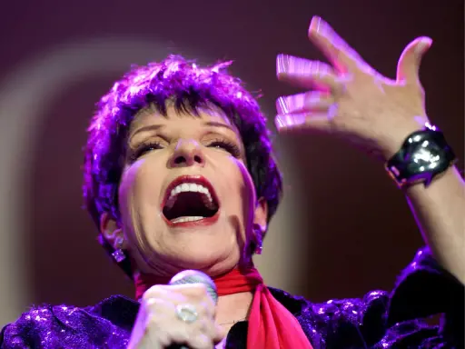 Liza Minnelli, en ikonisk artist, sjunger med passion på scenen, hennes ansikte upplyst av lila ljus.