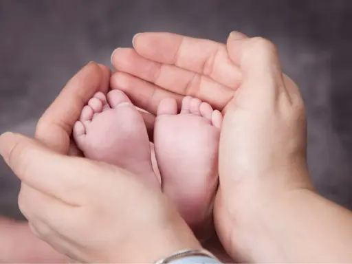 Manos adultas sostienen delicadamente los pies de un bebé. A partir de la semana 37, un bebé puede nacer.