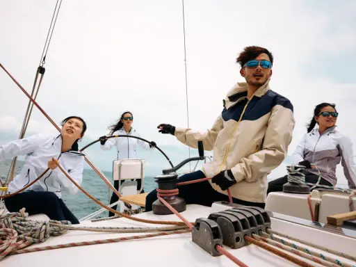 Kto to jest skipper? Młody mężczyzna w okularach przeciwsłonecznych kieruje jachtem, podczas gdy jego załoga pracuje przy linach.