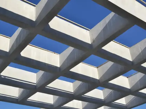 Estructura geométrica de vigas de hormigón armado, creando un patrón de cuadrados contra el cielo azul.