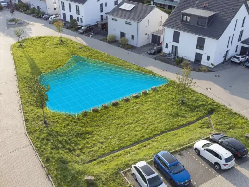 Eine blaue Fläche markiert eine geplante Mulde/Rigole in einem grünen Hang neben modernen Häusern und geparkten Autos.