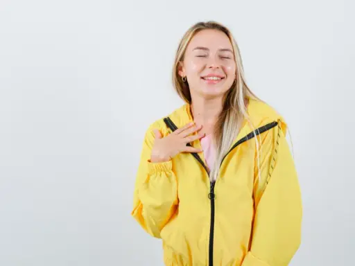 Uśmiechnięta blondynka w żółtej kurtce softshellowej, która przypomina jej, jak prać softshell, by zachować jego właściwości.