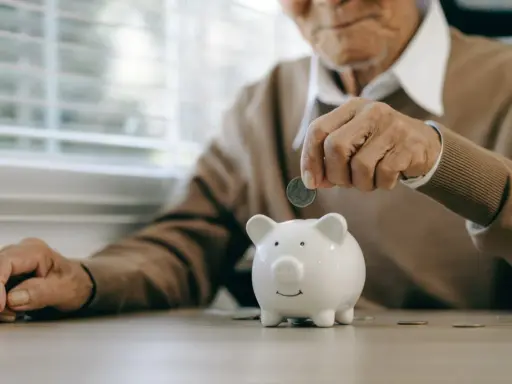 Un anciano deposita una moneda en una hucha, preparándose para la jubilación obligatoria.