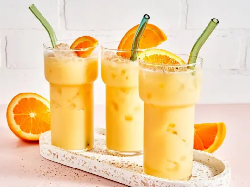 Drei cremige, eisgekühlte Painkiller Cocktails mit Orangenscheiben und grünen Strohhalmen auf einem Terrazzo-Tablett.
