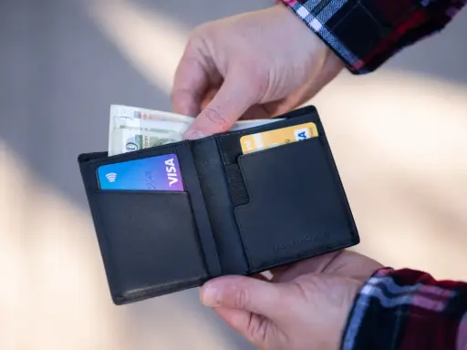Dłonie wkładają pieniądze i kartę Visa do czarnego portfela.