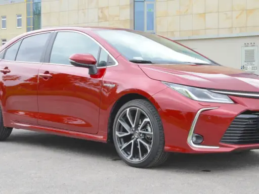 Błyszcząca, czerwona Toyota Corolla 1.8 Hybrid stoi na tle nowoczesnego budynku.