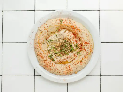 Cremiger Hummus-Dip mit Paprikapulver, Pinienkernen und Petersilie auf einem Teller, bereit zum Dippen.