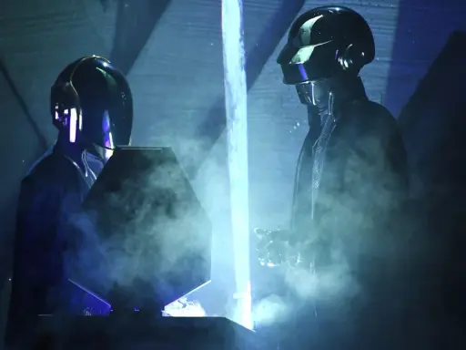 Medlemmar av Daft Punk i sina ikoniska hjälmar, omgivna av rök och blått ljus på scenen.