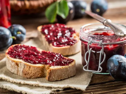 Frisches Brot mit Pflaumenmarmelade ohne Zucker, daneben eine Einmachglas gefüllt mit der leckeren Marmelade und frische Pflaumen.