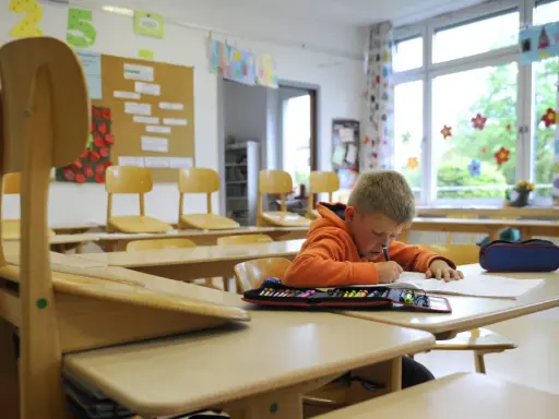 Ein Junge lernt allein im Klassenzimmer. Die leeren Stühle erinnern an eine kollektivstrafe, die er nicht verdient hat.