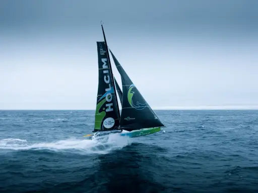 Segelboot des **Team Holcim** pflügt durch die Wellen, die Segel sind mit dem Logo und "The Ocean Race" beschriftet.