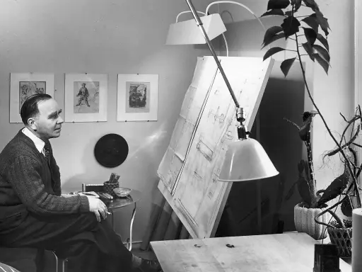 Paavo Tynell sitter vid sitt ritbord, omgiven av sina skisser och en stor ritning.