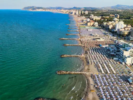 Vista aerea della costa adriatica, con la spiaggia affollata di ombrelloni e stabilimenti balneari, che si estende fino a Cattolica e Misano.