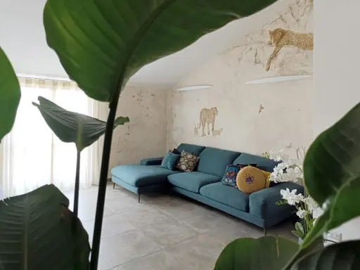 Divano turchese in un salotto con carta da parati a tema giungla e piante rigogliose, per un perfetto **stile jungle chic**.