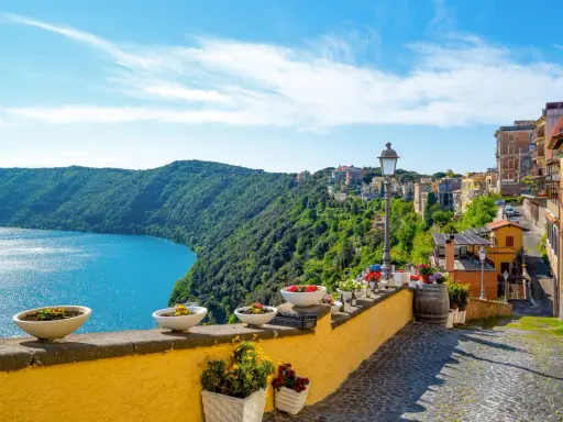 Widok na jezioro i zielone wzgórza z kolorowymi domami w Castel Gandolfo.