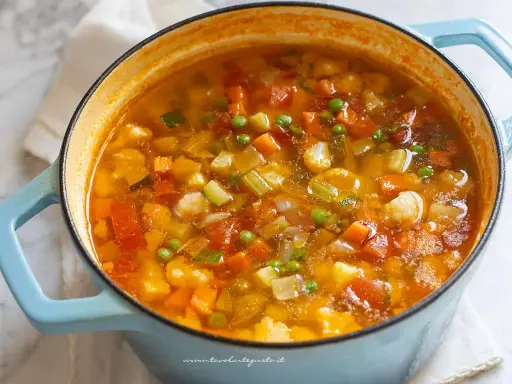 Un fumante minestrone di verdure in una pentola azzurra, ricco di carote, zucchine, piselli e pomodoro.