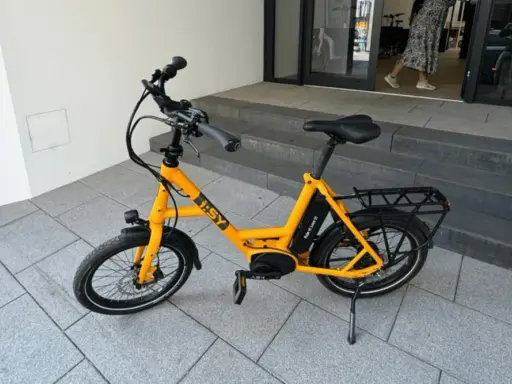 Gelbes i:SY E-Bike, das bei der Stiftung Warentest gut abgeschnitten hat, steht auf gepflastertem Untergrund vor einer Treppe.