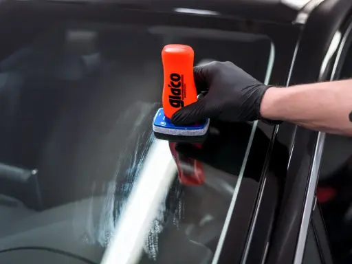 Rękawiczka z czarną rękawiczką nakłada preparat na szybę. To pokazuje, jak działa powłoka hydrofobowa, co to znaczy, że woda spływa.