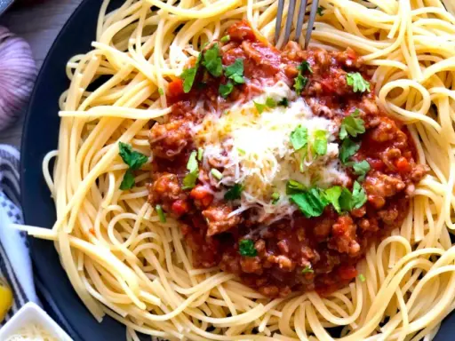 Spaghetti bolognese, prosty przepis. Aromatyczny sos mięsny z mielonym mięsem i pomidorami na złocistym makaronie, posypany serem i natką pietruszki.