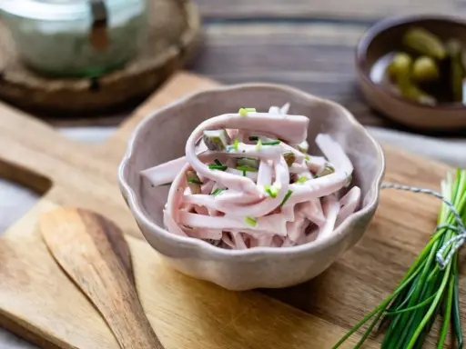 Schmackhaftes Fleischsalat Rezept mit Gurkenstückchen und Schnittlauch garniert, serviert in einer Schale auf einem Holzbrett.