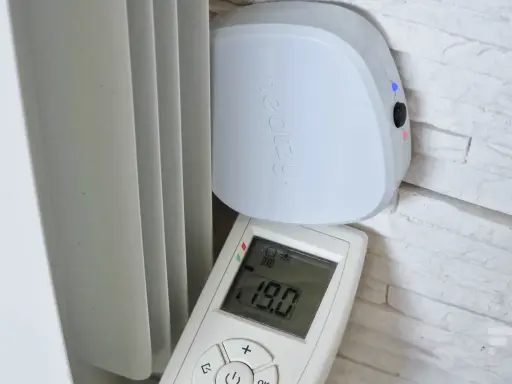Schéma branchement thermostat chauffage électrique : un boîtier blanc "heatzy" et une télécommande affichant 19.0°C, près d'un radiateur.