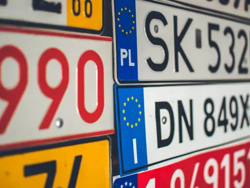 Stos tablic rejestracyjnych, w tym polskie z symbolem PL i europejską gwiazdką. Widać numery takie jak 990, SK 532HH, DN 849XJ.
