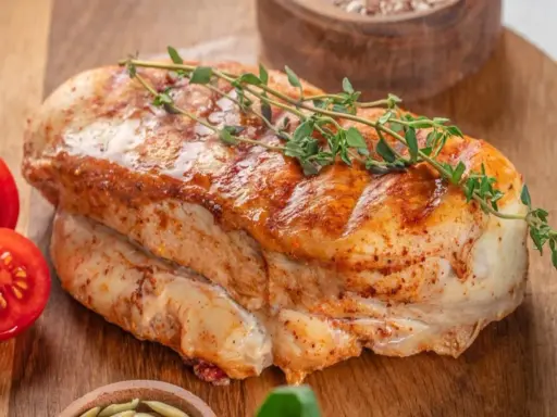 Soczysty filet z indyka, pieczony z ziołami, podany z pomidorkami koktajlowymi na drewnianej desce.