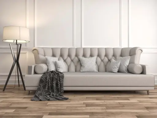 Divano imbottito grigio con cuscini a righe e coperta geometrica. La luce soffusa di una lampada da terra illumina la scena, dimostrando come grigio e beige stiano bene insieme.
