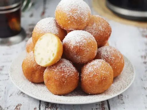 Puszyste pączki z piekarnika, posypane cukrem pudrem, kuszą swoim wyglądem. Jeden przekrojony ukazuje idealnie wyrośnięte wnętrze.